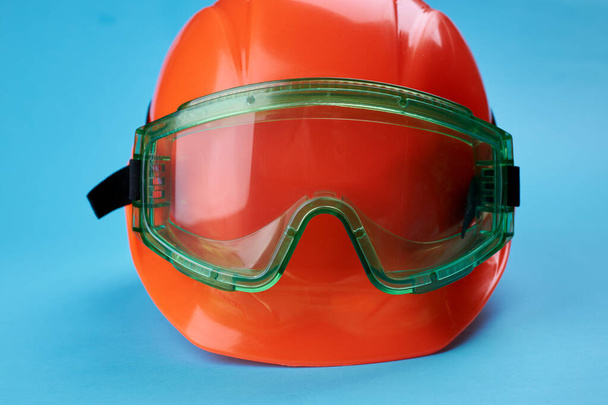 casque de protection orange et des lunettes de sécurité près de lui sur un fond bleu vif. Vêtements de travail et construction concept de l'industrie - Photo, image