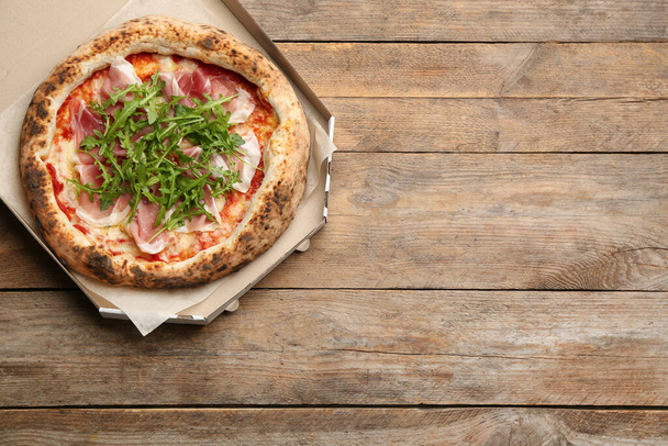 Tasty pizza with meat and arugula in cardboard box on wooden table, top view. Space for text - Fotografie, Obrázek