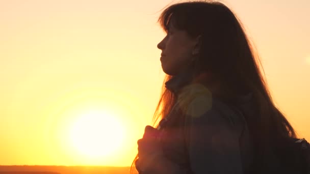 Meisjesreiziger met een rugzak bij zonsondergang kijkt in de lucht en bidt. Een vrouw droomt van een prachtig leven. Avonturier in het bos wandelen. Weekendwandelingen in het park - Video