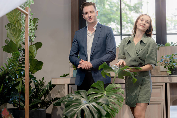 Muotokuva onnellinen liikemies ja nainen tarkistaa ja hoitaa vihreitä puita kasvi lehdet sisätiloissa rakennuksen puutarhassa. Konsepti toimistotilaa biofiliaa luonto. - Valokuva, kuva