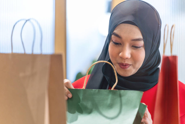 χαρούμενο πρόσωπο μουσουλμάνα γυναίκα σε κόκκινο φόρεμα έλεγχο τσάντες ψώνια. Concept άνθρωποι δραστηριότητα στην εμπορική περίοδο φεστιβάλ Χριστούγεννα και το νέο έτος. - Φωτογραφία, εικόνα