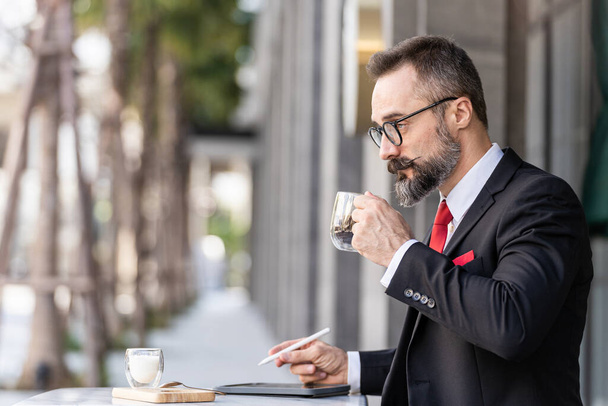 hombre mayor en traje de negocios inteligente pensando y sentado en la mesa de café al aire libre. - Foto, Imagen