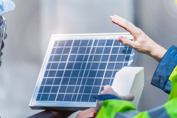 Fabrika işçisi teknisyenleri güneş pili panelini çalışan kask ve giysi ile sürdürülebilir teknoloji için gösterip kontrol ediyorlar. Konsept inşa fotovoltaik paneli yenilenebilir enerji yükle. - Fotoğraf, Görsel