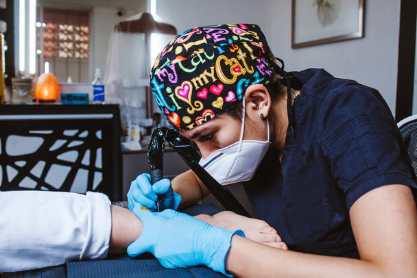 Latinská žena tetování umělec demonstruje proces získávání tetování s barvou a pracuje v modré sterilní rukavice v Mexico City - Fotografie, Obrázek