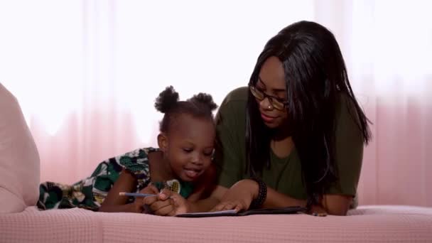 Šťastná rodina africká matka a dítě studují spolu, zatímco leží v posteli v ložnici. Afričanky dívka kreslení, když maminka učí ji. - Záběry, video
