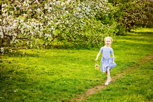 Hermosa chica en un huerto de manzanas en flor disfrutando de un cálido día de primavera. Un niño camina por el camino con una cesta en las manos. - Foto, imagen