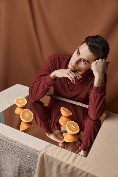 cut oranges on a mirror and a man at a table on a fabric background top view - Fotoğraf, Görsel