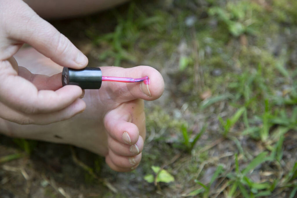 Nő festi a lábujját rózsaszín körömlakk a fűben - Fotó, kép