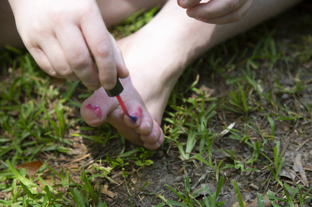 Mujer descuidadamente pintando sus dedos de los pies con esmalte de uñas rosa en la hierba - Foto, Imagen