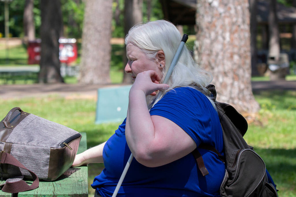 Mujer albina relajándose en un banco del parque, con una mochila en los hombros y una maleta abierta sobre la mesa - Foto, Imagen