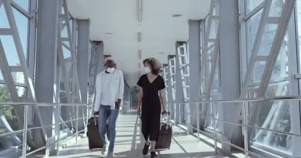 Images complètes couple afro-américain amis collègues masques médicaux et avec des valises marcher à travers la gare de l'aéroport pour atterrir avion arrivent en voyage d'affaires pendant la pandémie - Séquence, vidéo