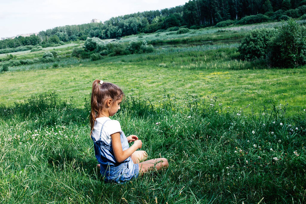 Onnellinen pieni tyttö istuu ja nauttia luonnosta nurmikolla. Lasten partiointi ja matkailun käsite. - Valokuva, kuva