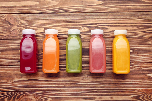 Fresh smoothies in plastic bottles on brown wooden background - Foto, afbeelding