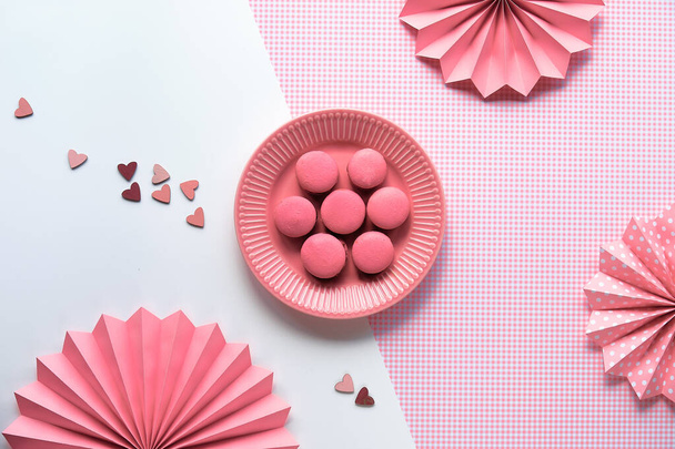Creative food concept. Sweet pink macaroons on a plate. Monochrome flat lay on split two tone pink white background with folded paper fans. - Фото, зображення