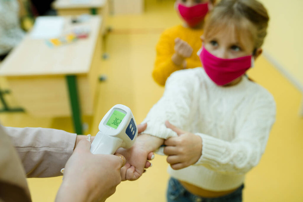 The teacher uses a non-contact thermometer to identify sick children. Training during a pandemic - Foto, Bild