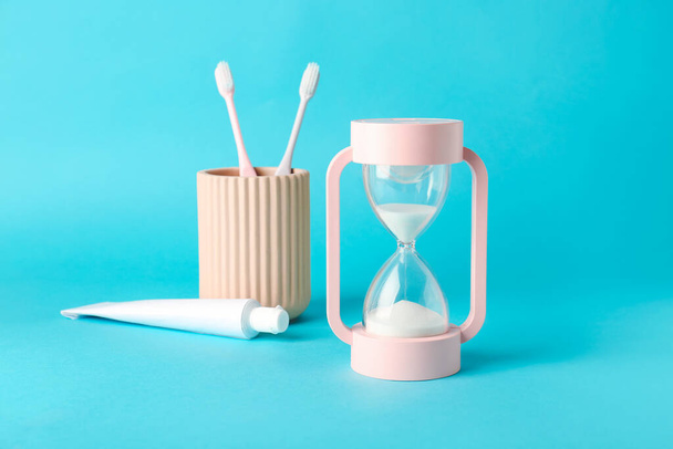 Hourglass, paste and toothbrushes on color background - Valokuva, kuva