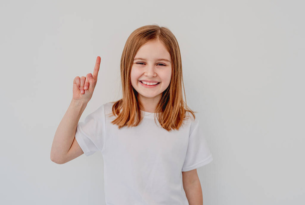 Happy little girl pointing upwards with finger - Fotó, kép