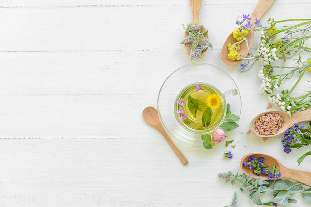 Flores, cucharas y taza con té floral sobre fondo claro - Foto, imagen