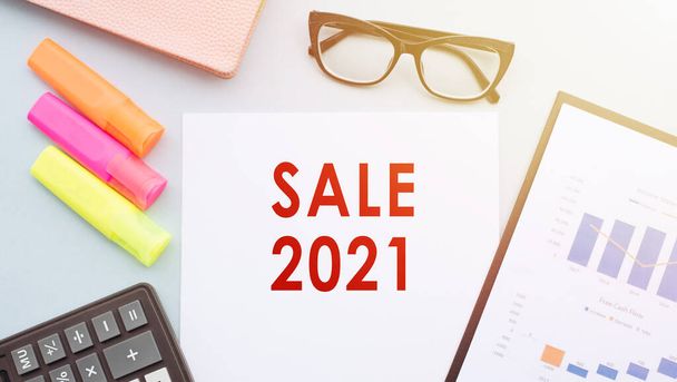 The text - SALE 2021 on office desk with calculator, markers, glasses and financial charts. - Foto, Imagem