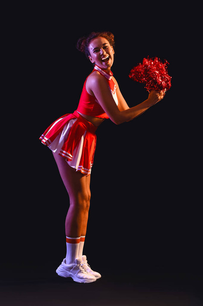 Beautiful young cheerleader on dark background - Photo, image