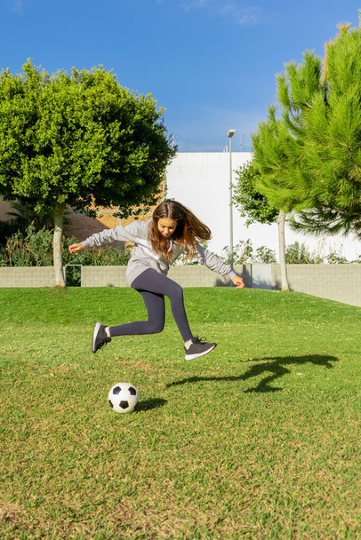 Krásná holčička hraje fotbal v pěkném parku s přirozenou trávou za slunečného zimního dne. Cvičení a zdravý život koncept - Fotografie, Obrázek