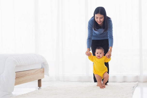 Asian little baby taking first steps learning to walk with mother help support the cute unstable walking toddler. Happy family first steps parenthood concept - 写真・画像