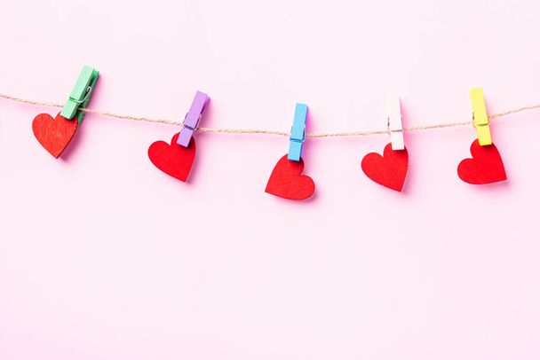 ハッピーバレンタインの日のコンセプト。赤いハート型のバレンタインの装飾は、コピースペースとピンクの背景に隔離されたロープに愛のための木のクリップでぶら下がっています - 写真・画像