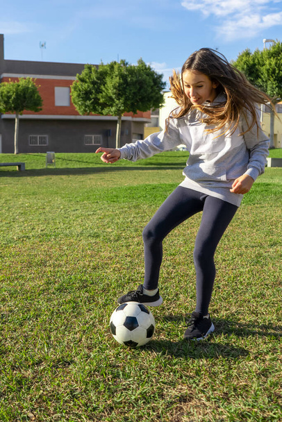 Όμορφο κοριτσάκι παίζει ποδόσφαιρο σε ένα ωραίο πάρκο με φυσικό χόρτο σε μια ηλιόλουστη μέρα του χειμώνα. Άσκηση και υγιεινή ζωή έννοια - Φωτογραφία, εικόνα