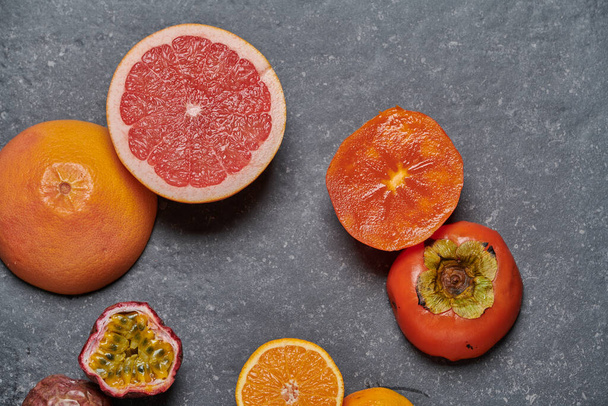 Draufsicht auf Orange mit Grapefruit, Granatapfel, Passionsfrucht und Kaki auf dunkelgrauem Hintergrund. Gesunde und frische Früchte zur Stärkung von Vitamin C und Immunsystem, von oben. - Foto, Bild