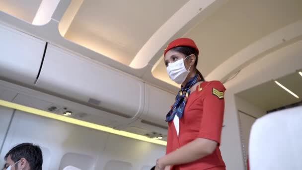 kobieta z maską na twarzy stewardesa lub personel pokładowy stoi i sprawdza siedzenia i wyposażenie pasażerów w samolocie. Koncepcja nowych podróży dla protokołów opieki zdrowotnej i zapobiegania pandemii wirusów. - Materiał filmowy, wideo