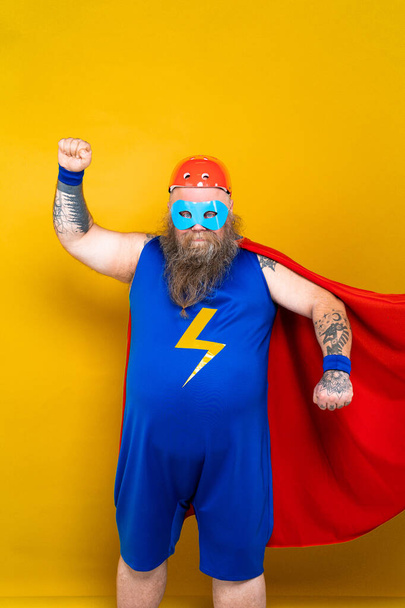 Funny fat man with superhero costume acting as superhuman with special powers, portrait on colored background - Φωτογραφία, εικόνα