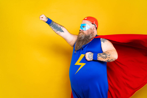 Funny fat man with superhero costume acting as superhuman with special powers, portrait on colored background - Zdjęcie, obraz