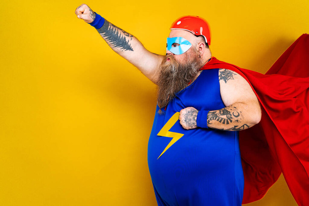 Funny fat man with superhero costume acting as superhuman with special powers, portrait on colored background - 写真・画像