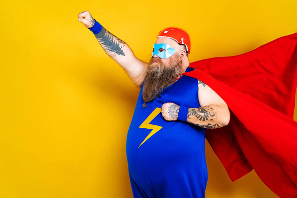 Funny fat man with superhero costume acting as superhuman with special powers, portrait on colored background - Photo, image