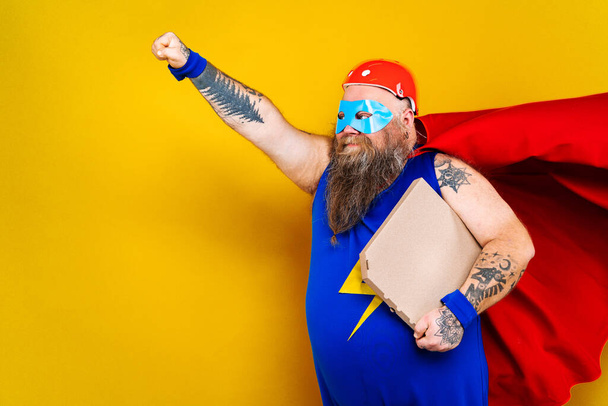 Funny fat man with superhero costume acting as superhuman with special powers, portrait on colored background - Photo, Image