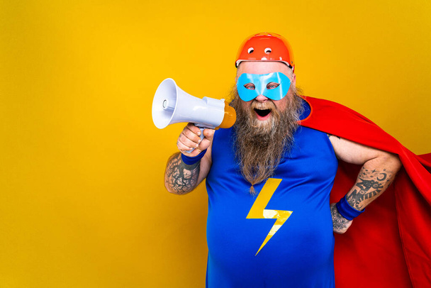 Funny fat man with superhero costume acting as superhuman with special powers, portrait on colored background - Photo, Image