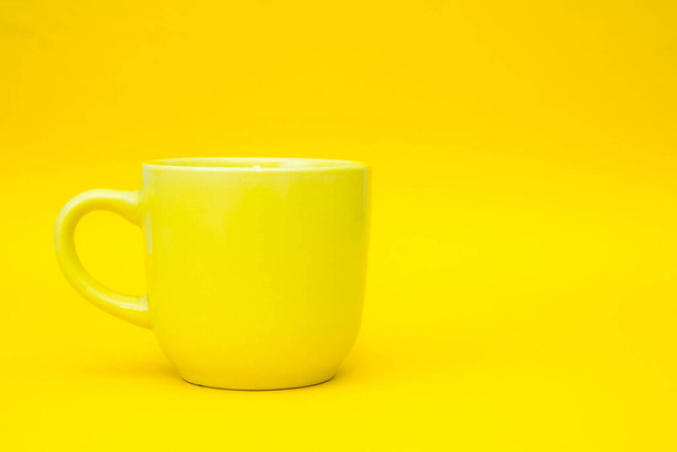 Gelbe Keramiktasse auf gelbem Hintergrund. Gelber Becher leer für Kaffee oder Tee. Raum für Text. - Foto, Bild