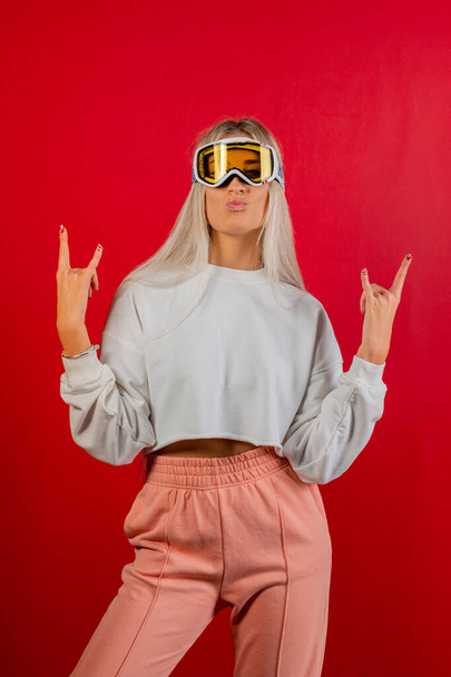 Portrait girl skier wearing glasses doing middle finger gesture. Close-up snowboarder on red background showing middle finger doing fuck you bad expression - Foto, Imagem