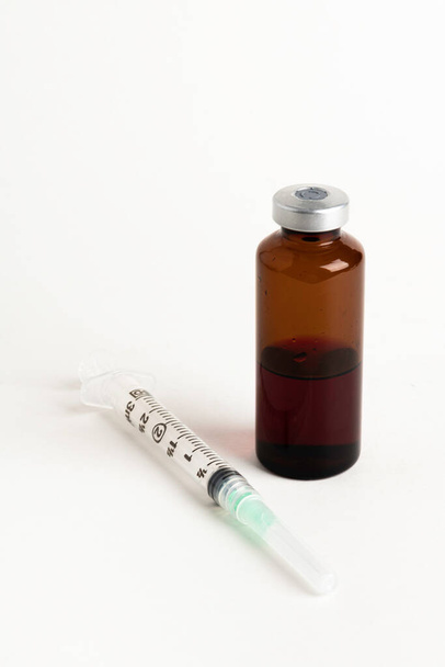 Detailní záběr hygienické jednorázové plastové injekce léku s jantarovou injekční lahvičkou na bílém pozadí. - Fotografie, Obrázek