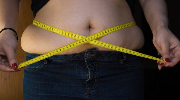 Фотографія пухкої дівчини з вимірювальною стрічкою навколо талії, щоб символізувати дієту
. - Фото, зображення
