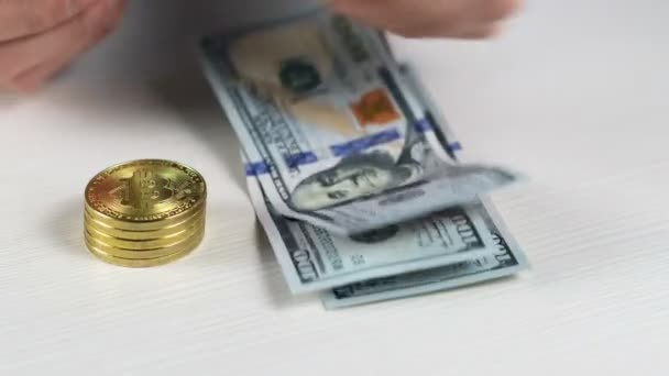Close-up, een man zet honderd dollar biljetten in een stapel op de tafel met zijn handen, een stapel Bitcoin munten staat in de buurt. - Video