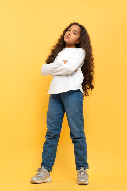 Full length portrait of young dark skinned African girl with curly hair wearing white shirt and jeans stands  on yellow  background. - Foto, Bild