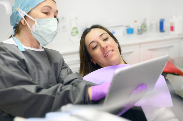 Concepto de cuidado de la salud - dentista femenina mostrando tableta a paciente mujer en la clínica dental. - Foto, Imagen
