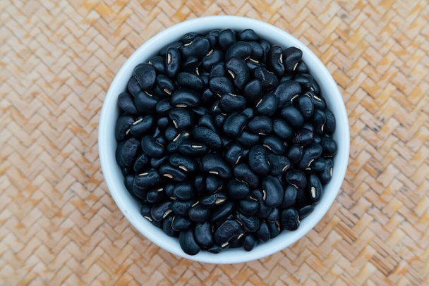Black beans in a white ceramic bowl, placed on a wooden tray. - Photo, Image