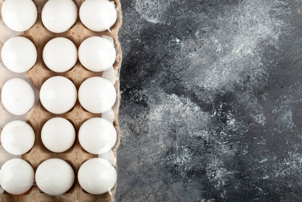 Сирі курячі яйця в яєчній коробці на мармуровому фоні
 - Фото, зображення