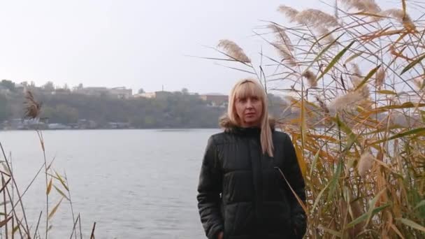 una mujer se para en la orilla del río en las cañas y piensa. estado de ánimo de otoño y depresión - Metraje, vídeo