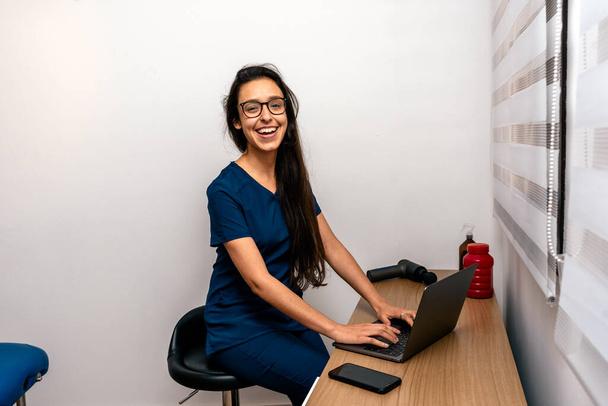 Photo de stock de femme heureuse portant un uniforme bleu avec téléphone et ordinateur portable souriant à la caméra. - Photo, image