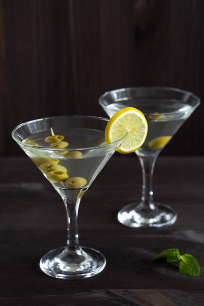 Два коктейля Маргариты в баре. бокалы мартини с оливками на деревянном фоне. Очки для мартини с лимоном и зеленой мятой на черном столе. скопировать пространство. алкогольные напитки. - Фото, изображение