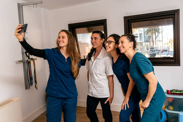 Foto de stock del equipo de trabajo unido de mujeres felices tomando selfie en la clínica de fisioterapia. - Foto, imagen