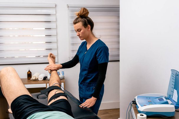 Stockfoto van een vrouwelijke werknemer die een man die in een brancard zit behandeling tegen pijn in zijn been geeft. - Foto, afbeelding
